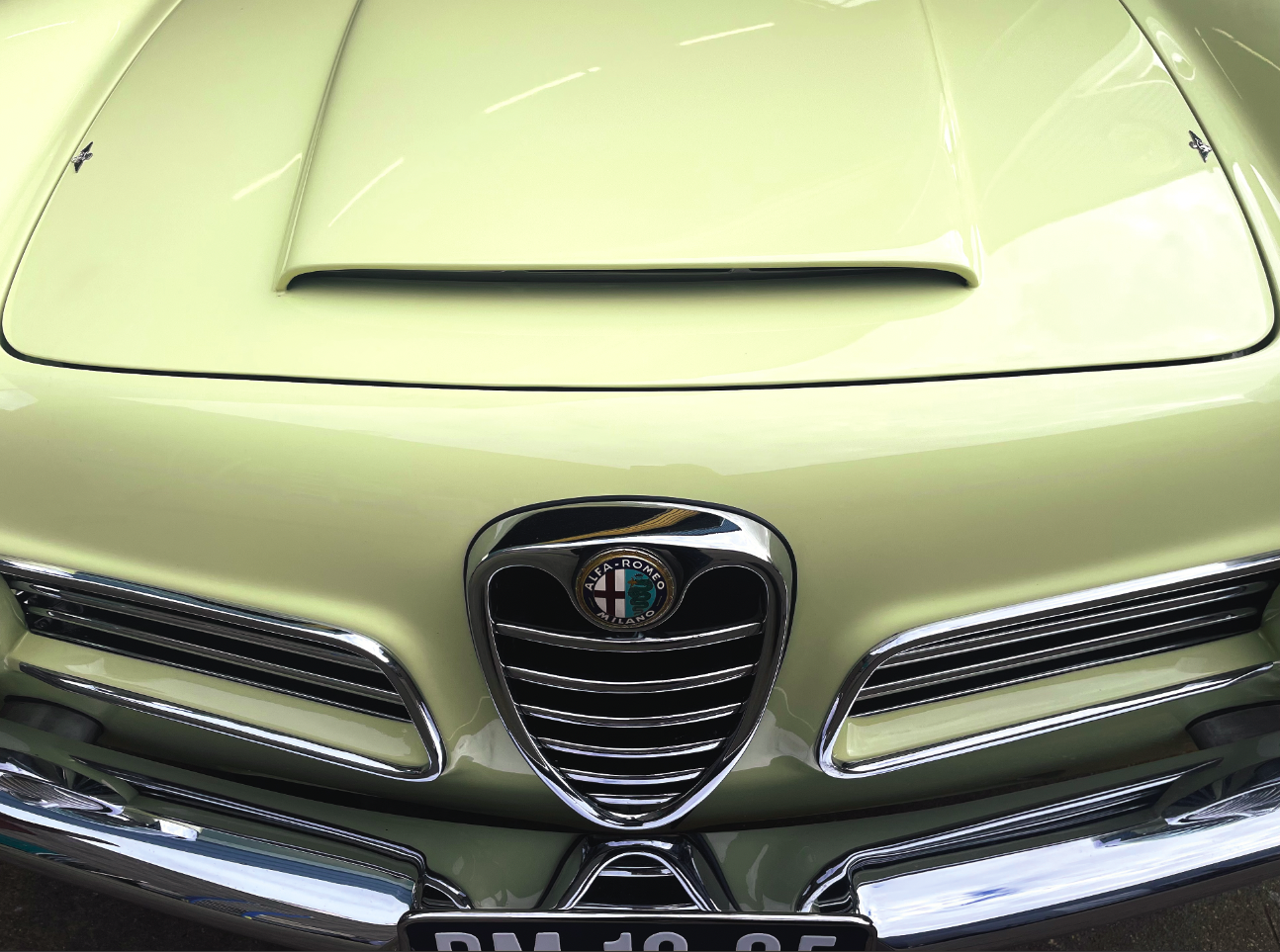 Close-up van het vooraanzicht van een klassieke Alfa Romeo met crèmekleurige lak, chromen bumper en merkteken